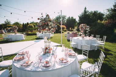 Yeşil çimenlikte ziyafet masası, dans pisti. Raflar, çatal bıçak takımı, kadife peçeteler, pembe bardaklar. Çiçeklerin çiçek aranjmanı. Gümüş şamdanlar ve mumlar. Masanın üzerinde beyaz bir masa örtüsü var..