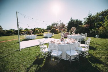 Yeşil çimenlikte ziyafet masası, dans pisti. Raflar, çatal bıçak takımı, kadife peçeteler, pembe bardaklar. Çiçeklerin çiçek aranjmanı. Gümüş şamdanlar ve mumlar. Masanın üzerinde beyaz bir masa örtüsü var..