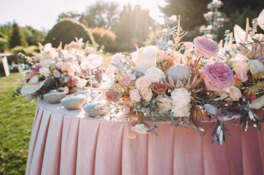 Presidium, yeni evlilerin masası. Çiçekli pembe güller, anthurium, protea, östoma, karanfiller, gümüş yapraklar. Masanın üzerinde pembe kadife bir masa örtüsü var. Yeşil çimlerin üzerinde