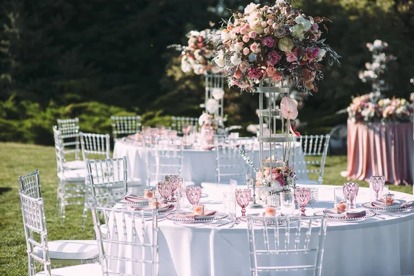宴席在绿色的草坪上 裤子和餐具 天鹅绒餐巾 粉色眼镜 粉红花朵的花朵排列 银制烛台和蜡烛 桌子上有一张白色桌布 — 图库照片