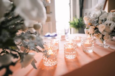 Presidyum, pembe masa örtülü ziyafet masası. Tabaklar, çatal bıçak takımı, mor bardaklar, peçeteler, cam şamdanlardaki mumlar. Çiçek buketi, asterler, güller, karanfiller, mutluluklar..