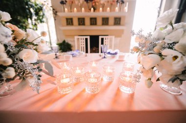 Presidyum, pembe masa örtülü ziyafet masası. Tabaklar, çatal bıçak takımı, mor bardaklar, peçeteler, cam şamdanlardaki mumlar. Çiçek buketi, asterler, güller, karanfiller, mutluluklar..