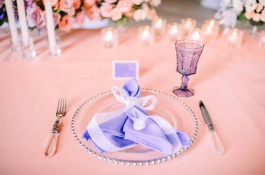 Presidyum, pembe masa örtülü ziyafet masası. Tabaklar, çatal bıçak takımı, mor bardaklar, peçeteler, cam şamdanlardaki mumlar. Çiçek buketi, asterler, güller, karanfiller, mutluluklar..