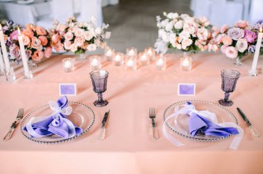 Presidyum, pembe masa örtülü ziyafet masası. Tabaklar, çatal bıçak takımı, mor bardaklar, peçeteler, cam şamdanlardaki mumlar. Çiçek buketi, asterler, güller, karanfiller, mutluluklar..