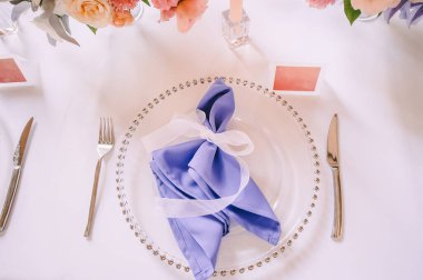 Presidyum, beyaz masa örtülü ziyafet masası. Tabaklar, çatal bıçak takımı, mor bardaklar, peçeteler, cam şamdanlardaki mumlar. Çiçek buketi, asterler, güller, karanfiller, mutluluklar..