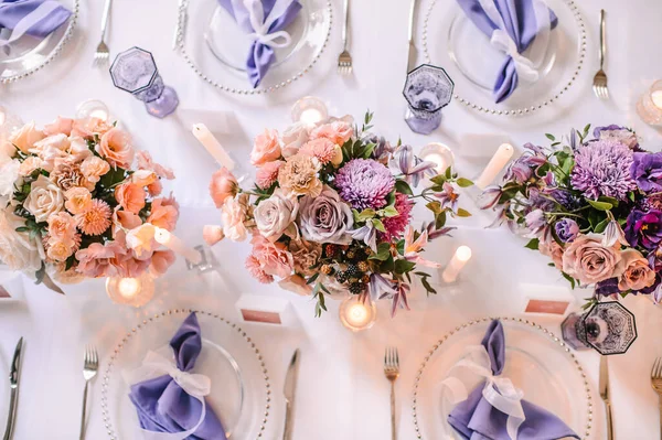 用白色桌布装饰的宴席 盘子和餐具 紫色眼镜 玻璃烛台上的蜡烛 康乃馨 — 图库照片