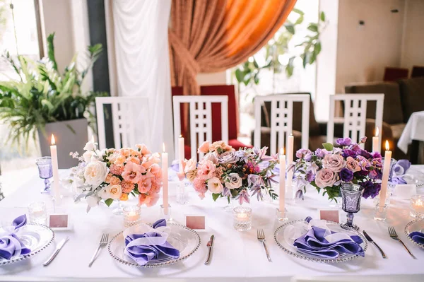 用白色桌布装饰的宴席 盘子和餐具 紫色眼镜 玻璃烛台上的蜡烛 康乃馨 — 图库照片
