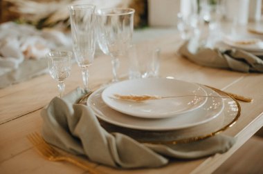 Taşralı. Ahşap ziyafet masası: Tabaklar, çatal bıçak takımı, keten peçeteler, kristal bardaklar, masa numarası olan oturma kartları.