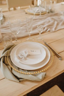 Taşralı. Ahşap ziyafet masası: Tabaklar, çatal bıçak takımı, keten peçeteler, kristal bardaklar, masa numarası olan oturma kartları.