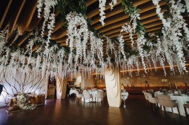 Modern ahşap arka plan, çelenk, iç mekan. Masalar servis edildi, çiçekler ve yeşillik kompozisyonları. Tabaklar, çatal bıçak takımı, peçete, pembe bardaklar. Yemek salonu..