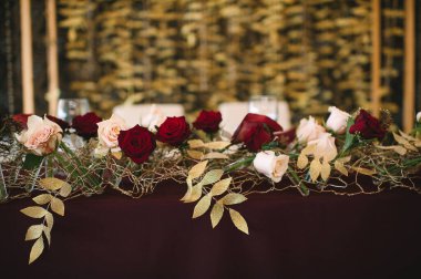 Presidyum, marsala masa örtülü ziyafet masası, mumlar, set kartları, peçeteler, tabaklar, çatal bıçak takımı, bardaklar, marsala gülünün çiçekleri. Mumlar, altın dekoru, şarap ve marsala renkleri.