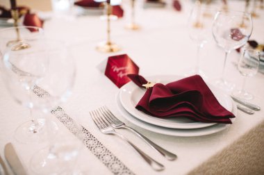 Beyaz masa örtülü ziyafet masası, mumlar, set kartları, peçeteler, tabaklar, çatal bıçak takımı, bardaklar, marsala gülünden çiçekler. Mumlar, altın dekoru, şarap ve marsala renkleri.