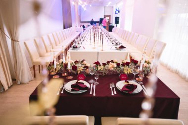 Marsala masa örtülü ziyafet masası, mumlar, set kartları, peçeteler, tabaklar, çatal bıçak takımı, bardaklar, marsala gülünden çiçekler. Başlık: 