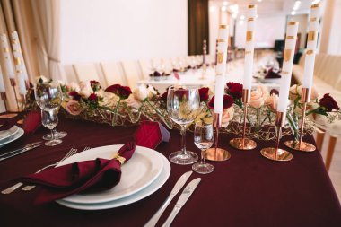 Marsala masa örtülü ziyafet masası, mumlar, set kartları, peçeteler, tabaklar, çatal bıçak takımı, bardaklar, marsala gülünden çiçekler. Mumlar, altın dekoru, şarap ve marsala renkleri.