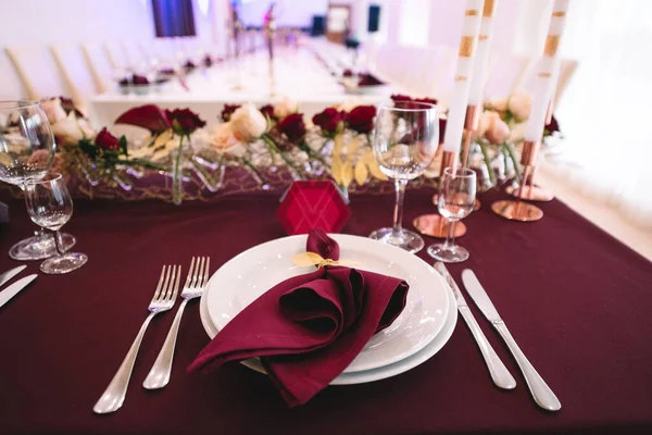 Marsala masa örtülü ziyafet masası, mumlar, set kartları, peçeteler, tabaklar, çatal bıçak takımı, bardaklar, marsala gülünden çiçekler. Mumlar, altın dekoru, şarap ve marsala renkleri.