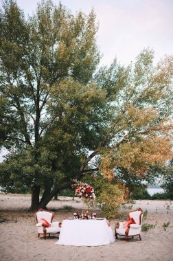 Doğayla ilgili bir ziyafet, beyaz masa örtülü bir masa, altın kenarlı klasik tabaklar, şarap bardakları, çatal bıçak takımı, mumlar, çiçeklerden oluşan bir kompozisyon, amirilis, güller, kırmızı yıldız çiçekleri..