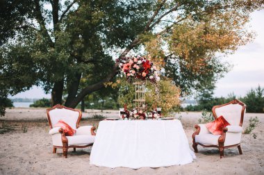 Doğayla ilgili bir ziyafet, beyaz masa örtülü bir masa, altın kenarlı klasik tabaklar, şarap bardakları, çatal bıçak takımı, mumlar, çiçeklerden oluşan bir kompozisyon, amirilis, güller, kırmızı yıldız çiçekleri..