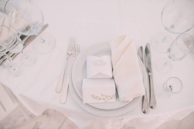 Restoran, ziyafet, sofra kurma. Masa beyaz bir masa örtüsü, bulaşıklar, beyaz temiz tabaklar, çatal bıçak takımı, peçeteler, şarap bardakları, mumlarla kaplı. Yakın plan..