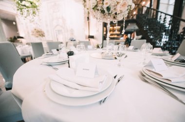 Restoran, ziyafet, sofra kurma. Masa beyaz bir masa örtüsü, bulaşıklar, beyaz temiz tabaklar, çatal bıçak takımı, peçeteler, şarap bardakları, mumlarla kaplı. Yakın plan..