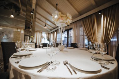 Restoran, ziyafet, sofra kurma. Masa beyaz bir masa örtüsü, bulaşıklar, beyaz temiz tabaklar, çatal bıçak takımı, peçeteler, şarap bardakları, mumlarla kaplı. Yakın plan..