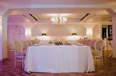 Restoran, iç mekan, ziyafet, masa düzenleme. Masa beyaz bir masa örtüsü, bulaşıklar, beyaz temiz tabaklar, çatal bıçak takımı, peçeteler, şarap bardakları, mumlarla kaplı. Genel plan.