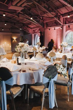 Restoran, iç mekan, ziyafet, masa düzenleme. Masa beyaz bir masa örtüsü, bulaşıklar, beyaz temiz tabaklar, çatal bıçak takımı, peçeteler, şarap bardakları, mumlarla kaplı. Genel plan.