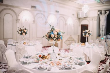 Restoran, ziyafet, sofra kurma. Masa beyaz bir masa örtüsü, bulaşıklar, beyaz temiz tabaklar, çatal bıçak takımı, peçeteler, şarap bardakları, mumlarla kaplı. Yakın plan..