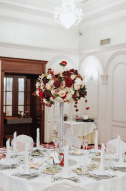 Restoran, ziyafet, sofra kurma. Masa beyaz bir masa örtüsü, bulaşıklar, beyaz temiz tabaklar, çatal bıçak takımı, peçeteler, şarap bardakları, mumlarla kaplı. Yakın plan..