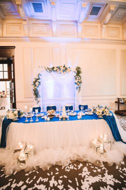 Presidyum, beyaz masa örtülü ziyafet masası, mumlar, set kartları, peçeteler, tabaklar, çatal bıçak takımı, bardaklar, çiçek kompozisyonu. 