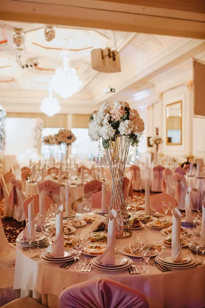 Restaurant, banquet, table setting. The table is covered with a white tablecloth, dishes, white clean plates, cutlery, napkins, wine glasses, candles. Close-up. Large crystal chandeliers