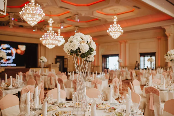 Restoran, ziyafet, sofra kurma. Masa beyaz bir masa örtüsü, bulaşıklar, beyaz temiz tabaklar, çatal bıçak takımı, peçeteler, şarap bardakları, mumlarla kaplı. Yakın plan. Büyük kristal avizeler.