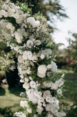 Açık havada düğün töreni. Taze beyaz çingene çiçekleri, güller ve yakın plan yeşillik ile süslenmiş düğün kemeri. Kutlama günü.