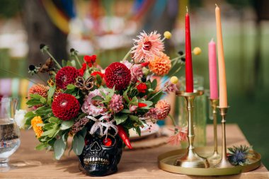 Çok renkli vazolarda, kafatası şeklinde vazolar, dekorda Meksika tarzı çiçekler. Düğün ziyafeti alanındaki şenlik masasında çiçekler ve yeşillik kompozisyonları, mumlar yerleştirilir..