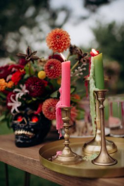 Çok renkli vazolarda, kafatası şeklinde vazolar, dekorda Meksika tarzı çiçekler. Düğün ziyafeti alanındaki şenlik masasında çiçekler ve yeşillik kompozisyonları, mumlar yerleştirilir..