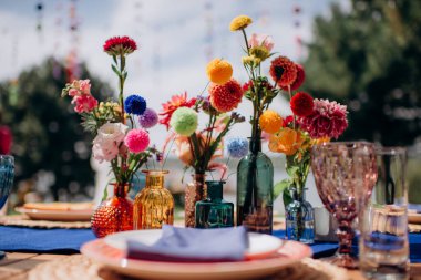 Vazolarda kırmızı çiçek aranjmanları, renkli dekorlar, sonbahar çiçekleri. Düğün ziyafeti alanındaki şenlik masasında çiçekler ve yeşillik kompozisyonları, mumlar yerleştirilir..