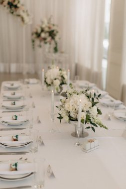 Gül, östoma ve cam vazolarda çeşitli çiçeklerle bir sürü küçük beyaz çiçek aranjmanı. Düğün ziyafeti alanındaki şenlik masasında çiçekler ve yeşillik kompozisyonları, mumlar yerleştirilir..