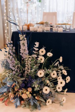 Yeni evlilerin masası için beyaz ve pembe çiçeklerden oluşan büyük bir çiçek aranjmanı, başkanlık makamının dekorasyonu. Düğün ziyafeti alanındaki şenlik masasında çiçekler ve yeşillik kompozisyonları, mumlar yerleştirilir..