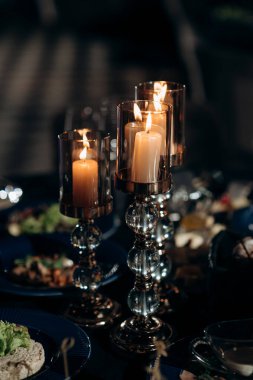 Düğün ziyafetinin olduğu bölgedeki şenlik masasında mumlar çiçek ve yeşillik karışımının şamdanlarına konur..