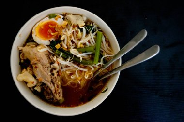 Şehriye, yumurta, sebze, domuz iskeleti, kaşık, yeşil kasede çatal ve kırpma yolu olan siyah ahşap arka plan ile görüntüyü terk etti. Hayat işte. Tayland ve yemek..