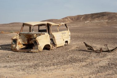 Kızgın gökyüzü ile çöl manzarasında hurda bir araba.
