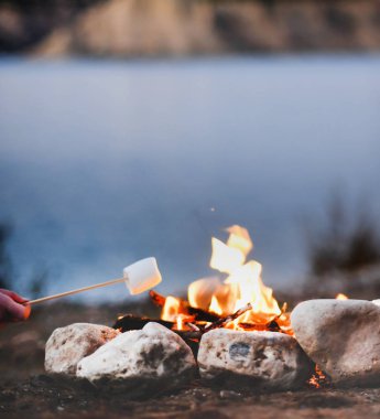kadın eli ön plan, kopya alanı odaklanmak için ateş bir göl kenarında kamp ise yaz sonu gecede bir kamp ateşi üzerinde Marshmallows kavurma metin yerleşimi için arka plan bulanık