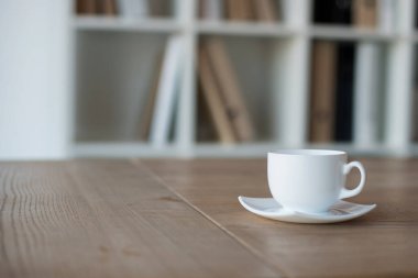 Ofisteki ahşap bir masanın üzerinde kahve fincanı ve fincan tabağı. Yumuşak odaklanma. Boşluğu kopyala