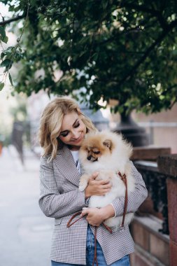 Pomeranian Spitz köpek cinsi köpeğiyle yürüyüşe çıkmış güzel sarışın bir kadın. Küçük tüylü köpek. Yumuşak seçici odak.