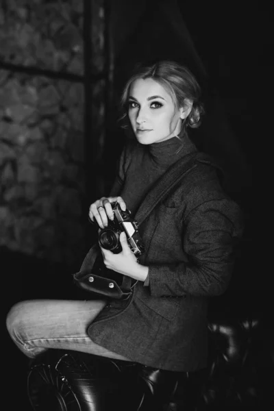 厳格なスーツの美しい女の子のブロンドの写真家は 彼の手に古いレトロなカメラを保持しています 白黒写真 — ストック写真