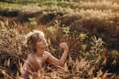 Özgürlük mutlu ve kıvırcık saçlı güzel kadın güneşli bir günde buğday tarlasında dinleniyor. Açık alan. Kadınların bağımsızlığı.