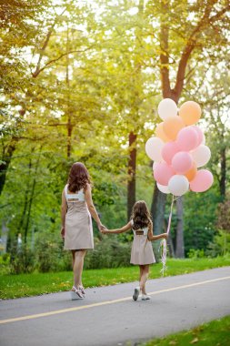 Anne ve kızı yazın bir sürü balonla parkta el ele yürüyorlar..
