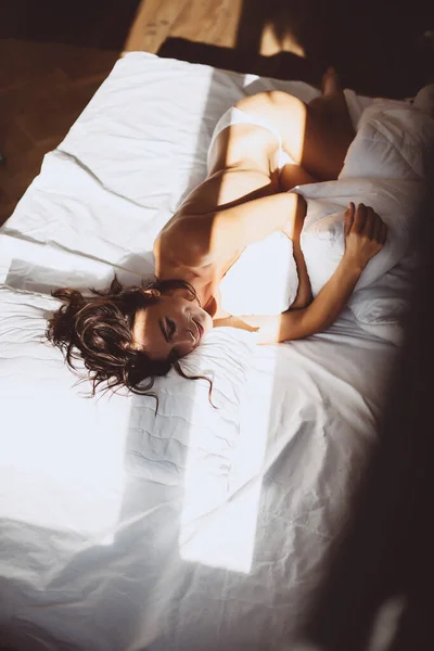 아름다운 소녀는 아침에 침대에 즐거운 미소를 지으며 일어나서 밖으로 베개를 — 스톡 사진