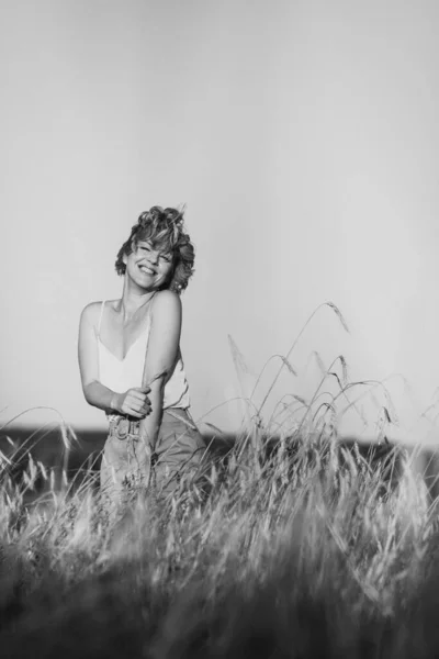 Freedom. A happy and beautiful woman with curly hair is dancing and smiling in the summer in a field with wheat on a sunny day. Open space. Black-white portrait.