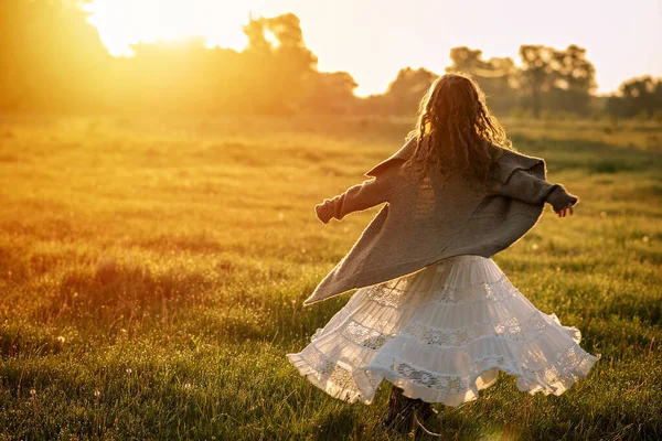 A little girl in a long dress dances in the grass in a field at dawn in the sun. Soft selective focus.