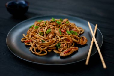 Tavuk sebzeli Asya udon eriştesi ve siyah ahşap arka planda çubuklarla teriyaki sosu. Çin ve Japon mutfağı.